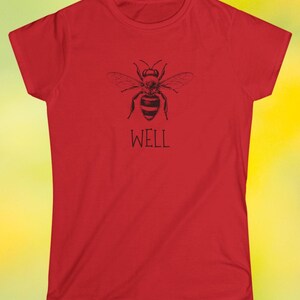 Op de afbeelding: Rood t-shirt met een zwarte bijenillustratie en het woord "WELL" eronder. Het ontwerp is gedrukt op een shirt met korte mouwen en een ronde hals, geschikt voor dagelijks gebruik.