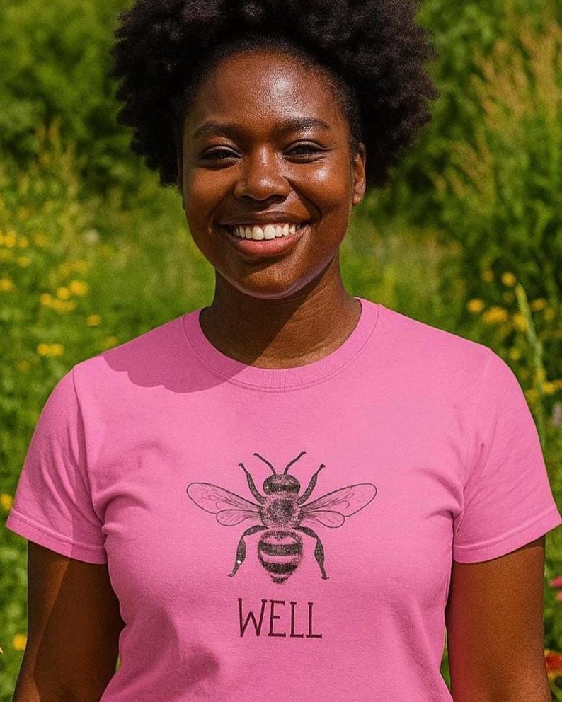 Op de afbeelding: Een roze T-shirt met een gedetailleerde zwart-witte illustratie van een bij en het woord "WELL" eronder. Het T-shirt heeft een ronde hals.