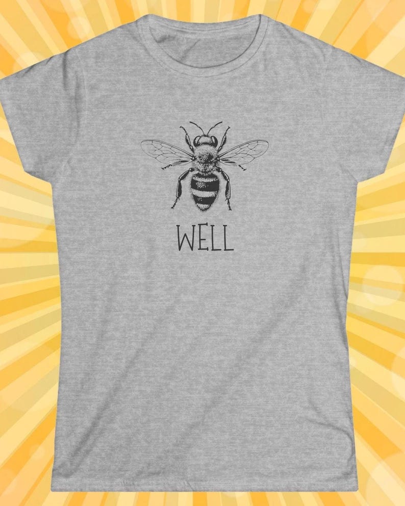 Op de afbeelding: Een lichtgrijs t-shirt met een zwart-witte illustratie van een bij met uitgespreide vleugels. Het woord "WELL" staat eronder in een eenvoudig lettertype. Het shirt heeft een ronde hals en korte mouwen.