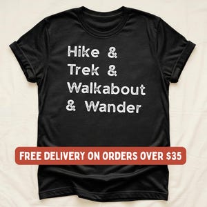 K&ouml;nnte beinhalten: Schwarzes T-Shirt mit wei&szlig;em Text "Hike & Trek & Walkabout & Wander". Die &Auml;rmel sind hochgekrempelt. Der Text ist in einem l&auml;ssigen, handschriftlichen Stil gehalten. Das T-Shirt besteht aus weichem Material.