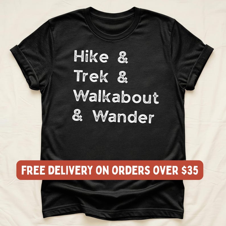 K&ouml;nnte beinhalten: Schwarzes T-Shirt mit wei&szlig;em Text "Hike & Trek & Walkabout & Wander". Die &Auml;rmel sind hochgekrempelt. Der Text ist in einem l&auml;ssigen, handschriftlichen Stil gehalten. Das T-Shirt besteht aus weichem Material.