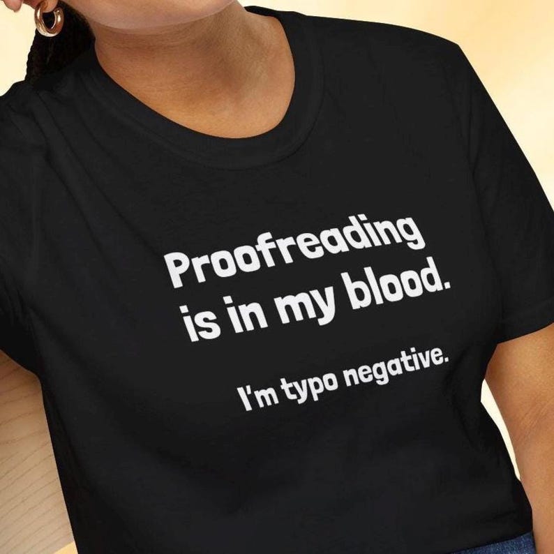 Pu&ograve; includere: T-shirt nero con la scritta bianca "Proofreading is in my blood. I'm typo negative." La maglietta ha un girocollo e maniche corte. Il testo &egrave; centrato sul davanti della maglietta.