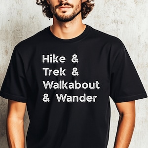 K&ouml;nnte beinhalten: Schwarzes T-Shirt mit wei&szlig;em Text: "Hike & Trek & Walkabout & Wander". Das Rundhals-T-Shirt ist aus weichem Material. Der Text ist mittig auf der Vorderseite. Ein l&auml;ssiges Oberteil f&uuml;r Outdoor-Enthusiasten.