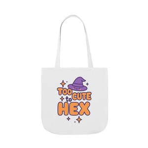 May include: White tote bag with a purple witch hat graphic and the text "Too Cute to Hex" in orange and purple. The bag has two white handles and is likely made of canvas or a similar material.