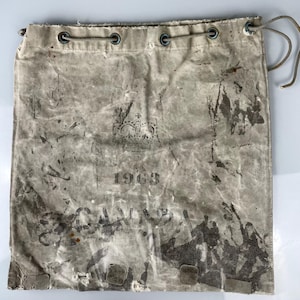 Può includere: Una borsa vintage in tela con chiusura a coulisse. La borsa è sbiadita e ha un aspetto usurato. La borsa ha una corona e l'anno 1968 stampato su di essa. La borsa è realizzata in tela spessa e resistente.