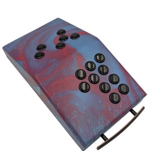 May include: A rectangular, marbled tray in shades of blue and red, featuring a series of black, circular buttons. The tray has a curved, black handle. The buttons are arranged in a pattern.