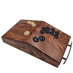 May include: A wooden arcade controller with black buttons and gold buttons. The controller has a dark wood grain finish.