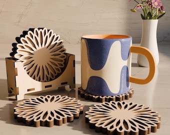 May include: Set of four wooden coasters with a floral design. The coasters are stacked in a holder and a blue and white mug is sitting on top of one of the coasters.