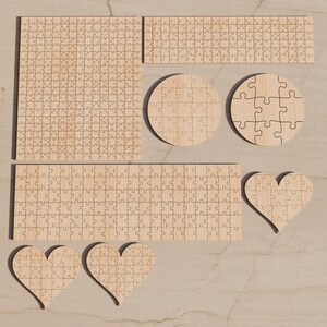May include: A collection of unfinished light wood jigsaw puzzles in various shapes, including one large square, one long rectangle, one shorter rectangle, two circles, and three heart shapes, all featuring interlocking puzzle piece cutouts.