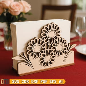 Könnte beinhalten: Ein Serviettenhalter aus Holz mit einem lasergeschnittenen Blumendesign. Der Halter hat drei große Blumen und Blätter mit einer hellen Holzoberfläche. Der Halter ist für eine Stapel Servietten konzipiert. Auf der Unterseite des Halters steht der Text "SVG CDR DXF PDF EPS AI".