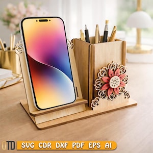 May include: Wooden desk organizer with a phone stand and pen holder. The phone is displayed in the stand. The pen holder has pens and pencils. A decorative flower is on the side. The base has the text "SVG CDR DXF PDF EPS AI".
