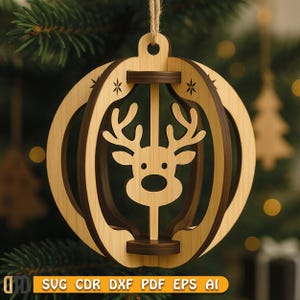 May include: A wooden Christmas bauble featuring a reindeer design. The bauble has a light brown outer layer and a darker brown inner layer, with a reindeer silhouette in the centre. It is suspended by a natural twine string.