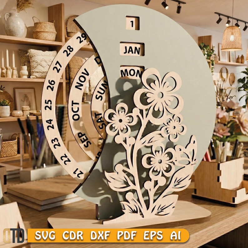 May include: A wooden perpetual calendar with a light green crescent-shaped background and a floral design. The calendar displays the month, day, and date. The base is made of light-colored wood. The text "JAN" and "MON" are visible.