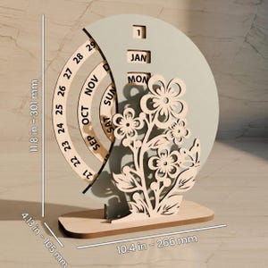 May include: A wooden perpetual calendar with a floral design. The calendar features a rotating date wheel, month and day blocks, and a decorative flower arrangement. The base is 10.4 inches (266 mm) wide and 4.13 inches (105 mm) tall, with an overall height of 11.8 inches (301 mm).