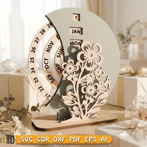 May include: A wooden perpetual calendar with a floral design. The calendar features a rotating ring for the days of the month, and blocks for the month and day. The base is rectangular, and the background is a light gray color.