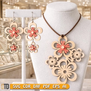 Könnte beinhalten: Ein Schmuckset bestehend aus einer Halskette und zwei Ohrringen aus hellem Holz. Die Kette hat ein braunes Band und einen Anhänger mit mehreren Blumenformen, während die Ohrringe aus zwei übereinanderliegenden Blütenausschnitten mit korallenfarbenen Zentren bestehen.