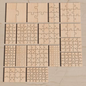 May include: A collection of fifteen light-colored wooden jigsaw puzzles of varying sizes and piece counts, arranged in a grid. Each puzzle features a distinct layout of interlocking pieces with dark, laser-cut lines visible on the smooth surface.