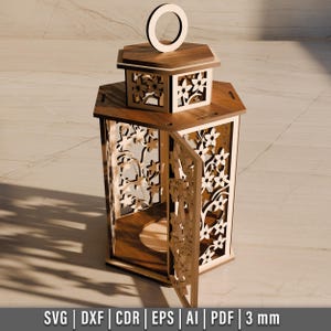 May include: A wooden lantern with intricate floral cutouts and a hinged door. The lantern features a handle at the top and is made of light brown wood. The design includes the text "SVG | DXF | CDR | EPS | AI | PDF | 3 mm".