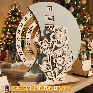 May include: A wooden perpetual calendar with a floral design. The calendar features rotating rings for the date and month, with the month of January and the day 1 visible. The design includes laser-cut flowers and leaves. The base is made of light-colored wood.