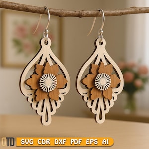 May include: Wooden dangle earrings with a floral design. The earrings feature a light wood teardrop shape with a layered brown flower and a white center. The earrings are hanging from a silver hook. The bottom of the image has the text "SVG CDR DXF PDF EPS AI".