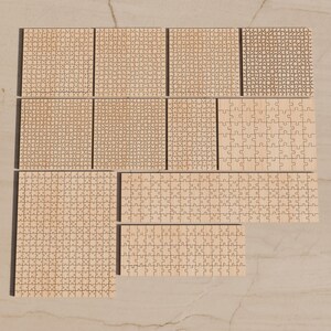May include: A collection of ten light-colored wooden jigsaw puzzles of varying sizes and piece counts, arranged in a grid-like formation. The puzzles feature natural wood grain textures and interlocking puzzle piece shapes.