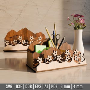 以下が含まれることがあります： 山脈のデザインと花のアクセントが施された木製デスクオーガナイザー。オーガナイザーには、ペン、鉛筆、その他のオフィス用品を収納できるスロットがあります。薄い茶色の木でできており、自然な仕上げになっています。