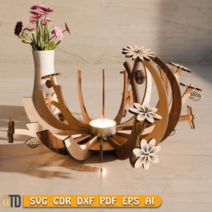 以下が含まれることがあります： 木製のキャンドルホルダー、花の模様。 ホルダーには、ろうそく用の中心スペースとピンクの花が入った花瓶があります。 デザインには、レーザーカットの花と葉のアクセントが含まれています。 ベースには「SVG CDR DXF PDF EPS AI」の文字があります。