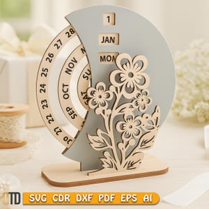 May include: A wooden perpetual calendar with a gray crescent-shaped background and a floral design. The calendar displays the date, month, and day. The base is rectangular. The text "SVG CDR DXF PDF EPS AI" is at the bottom.