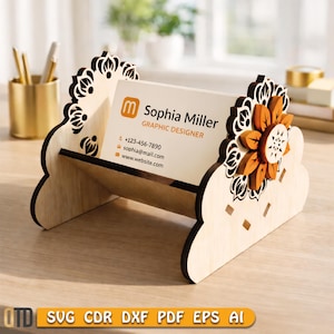 May include: A wooden business card holder with a floral design. The holder is made of light-coloured wood and features a laser-cut floral pattern on the sides and a decorative orange flower. The business card displays the name "Sophia Miller, Graphic Designer."