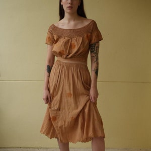 May include: A two-piece outfit in a light brown hue. The top features a crochet neckline and short sleeves, paired with a matching skirt. The skirt has a scalloped hemline. The outfit is made of a lightweight fabric.