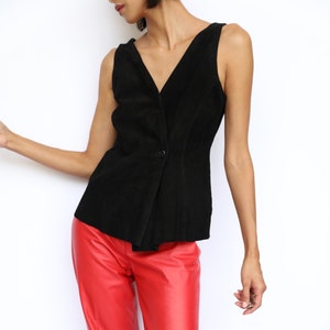 May include: A black sleeveless top with a V-neck and a single button closure, paired with bright red leather pants. The pants have a straight leg cut. The outfit is styled with patterned shoes.