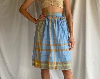 May include: A blue and yellow plaid skirt with a high waist and a gathered waistband. The skirt is knee-length and has a relaxed fit.