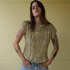 May include: A woman wearing a beige knitted sweater with a cable knit pattern and light blue denim shorts.