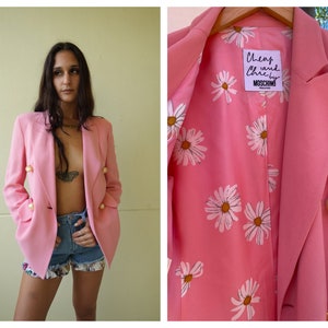 May include: A pink blazer with a daisy print lining and pearl buttons. The blazer has a label that reads "Cheap and Chic by Moschino".