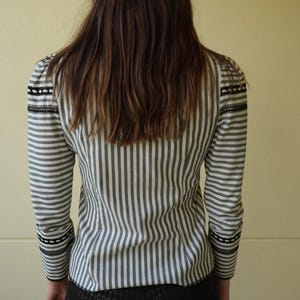 Pode incluir: Camisa de mangas compridas listrada em preto e branco. A camisa tem listras verticais, com acabamento preto nos ombros e punhos. As mangas s&atilde;o compridas e a camisa &eacute; abotoada.
