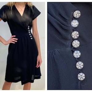 May include: A black wrap dress with short sleeves and a row of clear buttons down the side.