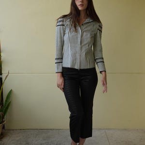 Pode incluir: Uma camisa listrada verticalmente em tons de cinza e branco, combinada com cal&ccedil;as pretas estampadas curtas. O conjunto &eacute; completado com sand&aacute;lias pretas. A camisa tem detalhes decorativos nos ombros e mangas.