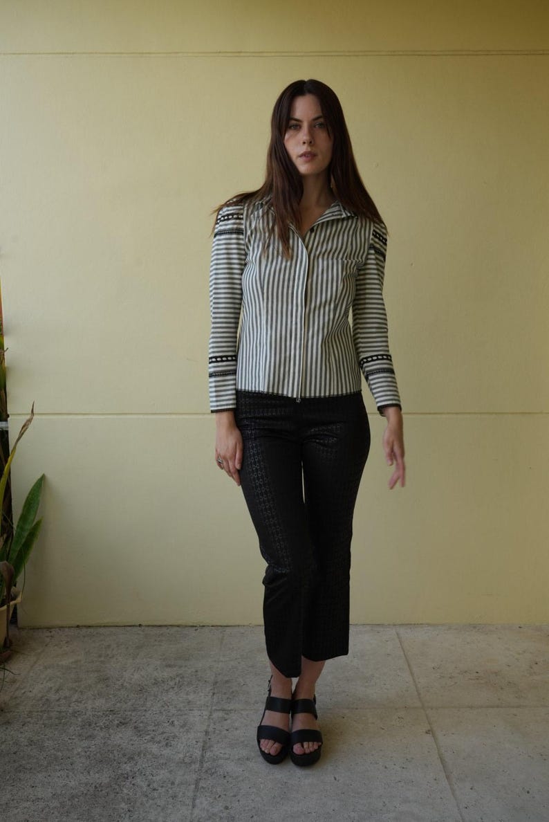 Pode incluir: Uma camisa listrada verticalmente em tons de cinza e branco, combinada com cal&ccedil;as pretas estampadas curtas. O conjunto &eacute; completado com sand&aacute;lias pretas. A camisa tem detalhes decorativos nos ombros e mangas.