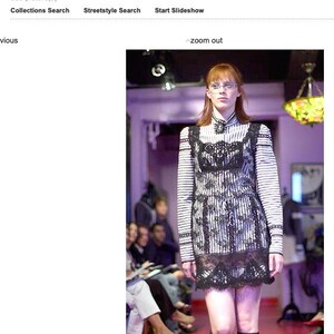 Pode incluir: Uma modelo numa passarela usando um vestido listrado em preto e branco com detalhes em renda preta. O vestido tem mangas compridas e gola alta. A passarela &eacute; vermelha e o fundo est&aacute; desfocado.