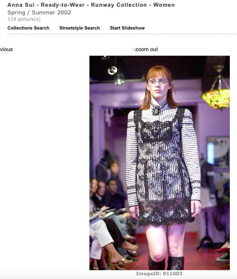 Pode incluir: Uma modelo numa passarela usando um vestido listrado em preto e branco com detalhes em renda preta. O vestido tem mangas compridas e gola alta. A passarela &eacute; vermelha e o fundo est&aacute; desfocado.