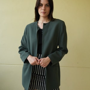 May include: A dark green blazer with a single button closure and long sleeves. The blazer is worn over a black top and a black and white striped skirt.