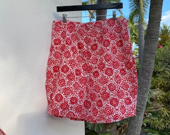 May include: A red and white floral print skirt hanging on a black hanger. The skirt is a mini length and has a fitted silhouette.