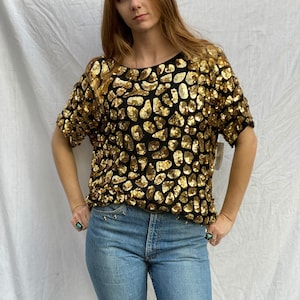 May include: A black short-sleeved top with a gold sequin pattern. The top has a round neckline and is made of a sheer fabric.