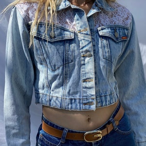 May include: A light blue denim jacket with a cropped hem and lace detailing on the shoulders. The jacket has a button closure and two front pockets.