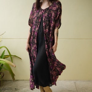 May include: A long, flowing floral print dress with a black slip underneath. The dress has a button-up front and short sleeves. The model is wearing tan cowboy boots.
