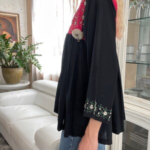 May include: Black tunic top with a pink and white floral embroidered bodice and sleeves. The top features a pleated skirt and a decorative embellishment at the waist. The sleeves are long and adorned with floral embroidery.