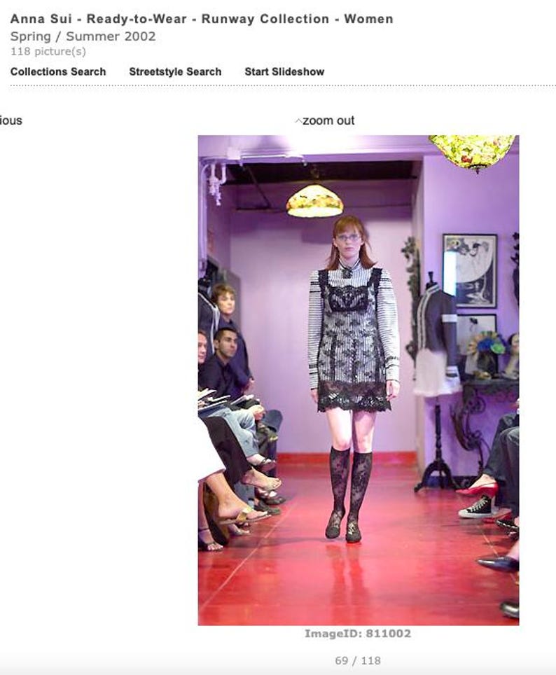 Pode incluir: Uma modelo com um vestido listrado em preto e branco com uma sobreposi&ccedil;&atilde;o de renda preta e meias pretas at&eacute; o joelho desfila em uma passarela vermelha. Imagem da cole&ccedil;&atilde;o Anna Sui Ready-to-Wear, Primavera/Ver&atilde;o 2002.