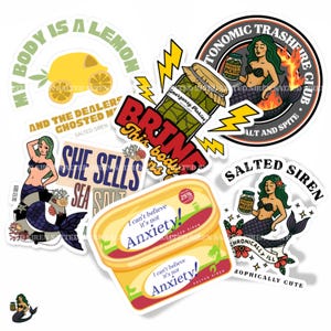 May include: A collection of colorful stickers with various designs. One sticker features a yellow lemon car, another says "She Sells Sea Salt", and others depict mermaids, pickles, and the text "Anxiety!"