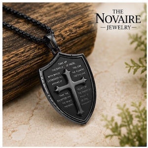 May include: A black metal pendant necklace featuring a shield-shaped charm with a central cross. The shield is engraved with the text: Take up the shield of faith, you can with which extinguish all the flaming arrows of the evil one. Take the helmet of salvation and the sword of the spirit which is the word of God.