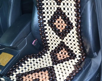 May include: A beaded car seat cover with a geometric pattern. The cover is made of small, light-colored, dark brown, and tan wooden beads. The cover is placed on a black car seat.